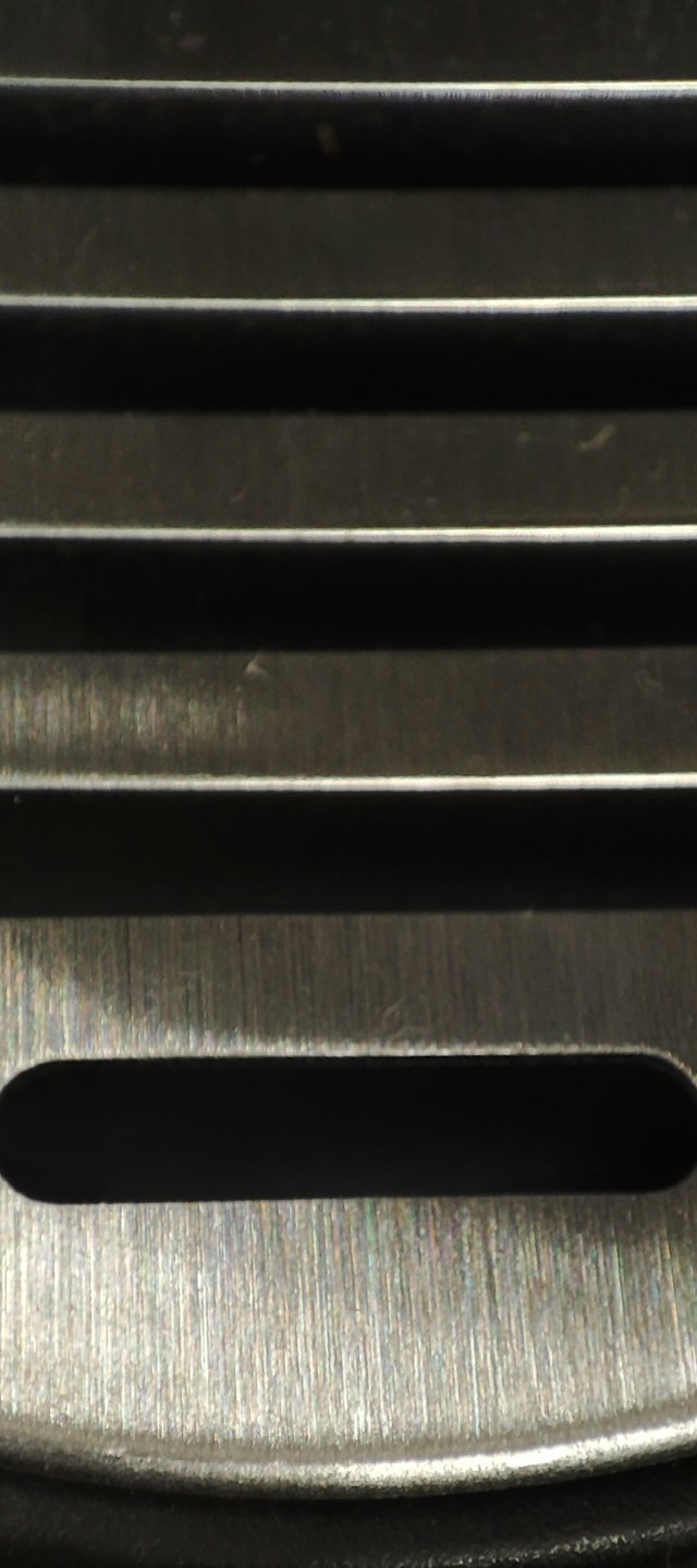 Tume harjatud metallpind horisontaalsete soonte ja kumera servaga.